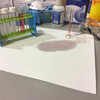Lab setup with test tubes, a dropper, and a piece of paper with a pink mark on a white pad