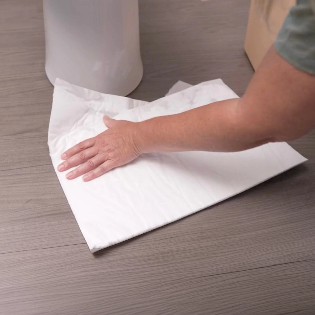 Person using a white paper pad on a wooden surface