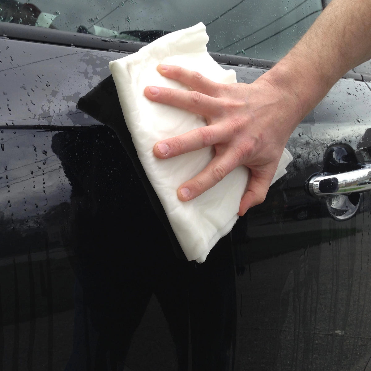 Person cleaning a car window with a white  pad